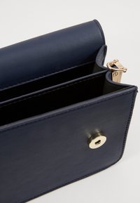 Portafoglio in pelle blu navy con una texture liscia, dotato di una chiusura in tonalità oro e due scomparti. Design pulito e rettangolare con accenti minimi.