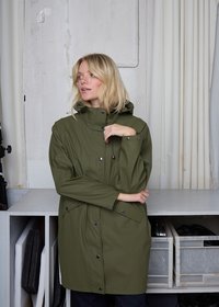 Alyvuogių žalia, neperšlampama striukė su kapišonu, spaudėmis ir šoninėmis kišenėmis; lygi tekstūra ir laisvas kirpimas, paprastame fone.