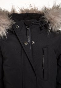 Parka negra con capucha con pelo, cierre frontal con cremallera, broches a presión y un bolsillo lateral. El material parece texturizado y duradero.