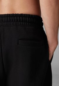 Black joggers with an elastic waistband, featuring a side pocket and a soft, textured finish. The design is simple and functional.