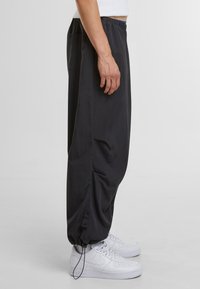 Zwarte, lichtgewicht, loszittende broek met een elastische tailleband, zijzakken en verstelbare boorden, gecombineerd met witte sneakers.