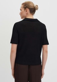 Zwart geribbeld gebreid top met korte mouwen, een kraaglijn, een gestructureerd oppervlak en een ontspannen pasvorm, gecombineerd met bruine broek.