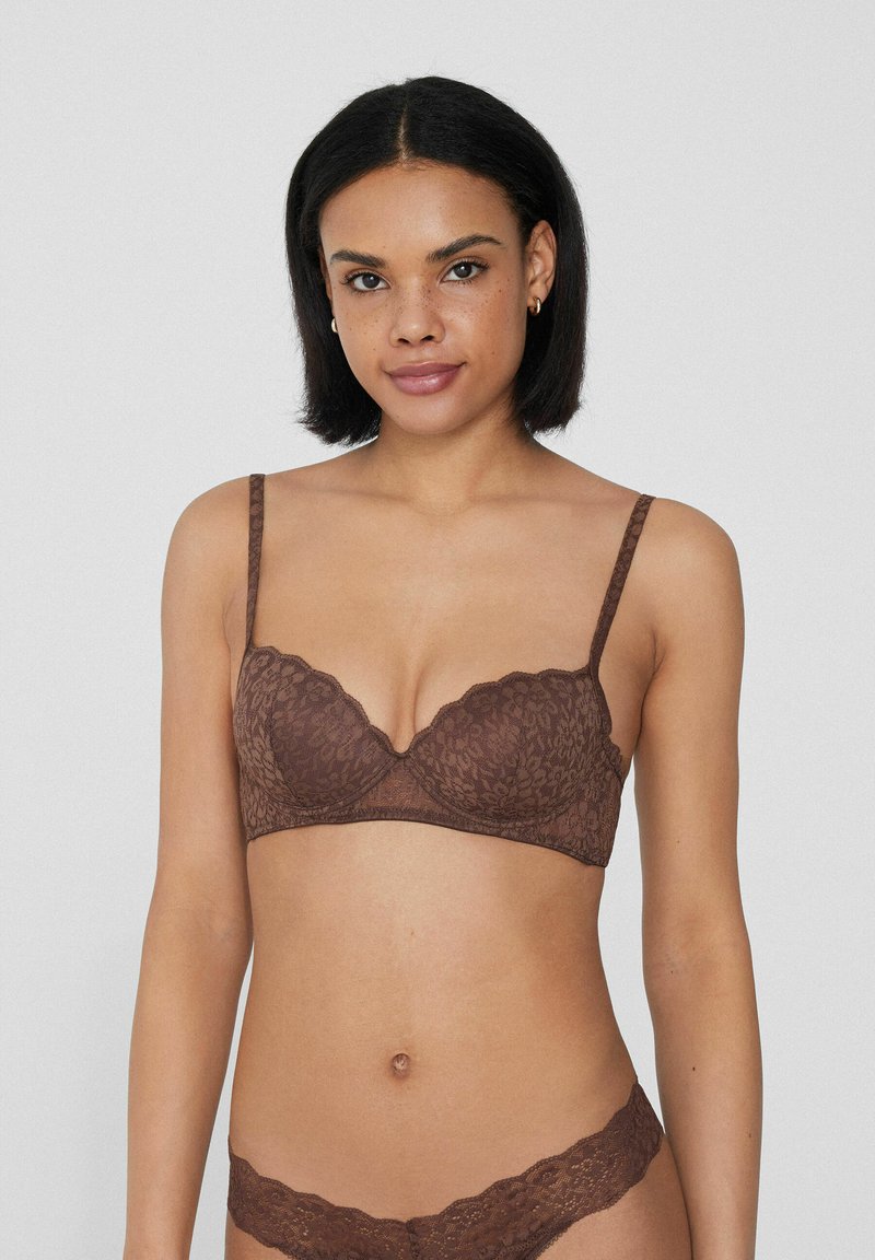 Brassière en dentelle marron avec des bords festonnés, des bretelles réglables et un motif floral, complétée par des culottes en dentelle assorties.