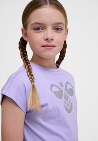 Lila Baumwoll-T-Shirt mit kurzen Ärmeln, das vorne ein glitzerndes graues Grafikdesign aufweist. Glatte Textur, taillierte Form.