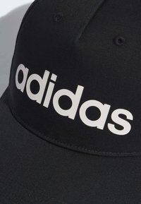 Gorra negra con visera curvada, hecha de tejido texturizado. Presenta un prominente logo blanco de "adidas" en la parte frontal. Dos agujeros de ventilación en la parte superior.