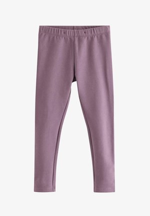 Barn med krøllet hår iført mørkebrun hættetrøje, hvid prikket skjorte, lilla leggings, lyserøde sokker og beige sko står mod hvid baggrund.