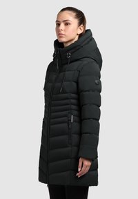 Čierny, podšitý dlhý kabát s kapucňou, obsahujúci zips, šnúrky a textúrované horizontálne prešívanie. S bočnými vreckami.