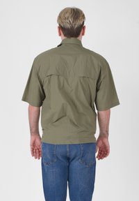 Camicia verde oliva a maniche corte con una vestibilità rilassata, caratterizzata da un dettaglio sul dietro. Abbinata a jeans in denim blu, vista da dietro.