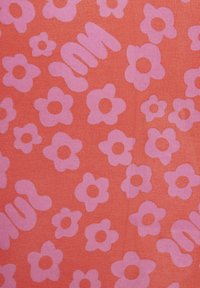 Tela roja cubierta de flores rosa claro y garabatos abstractos, creando un patrón juguetón. Textura suave y color uniforme.