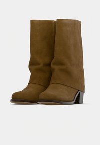 Barna velúr bokacsizmák laza dizájnnal, ferde sarokkal és sima felülettel. A hátsó része enyhén megemelt, és lekerekített orrú.