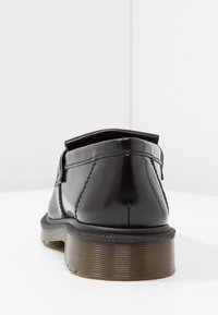 Chaussures en cuir verni noir avec un bout arrondi, des coutures contrastantes et une semelle marron texturée. Le design présente un talon bas et une esthétique minimaliste.