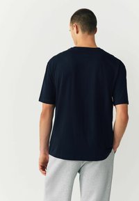 Lühikeste käistega tumehall t-särk, mis on valmistatud pehmest kangast, ümarate kaelustega ja laia lõikega, kantud heledate hallide pükste koosseisus.