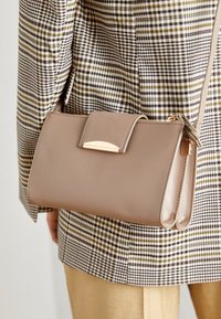 Sac à main synthétique beige avec fermeture plate, accessoires en ton or et bandoulière détachable, associé à un blazer à motif écossais.