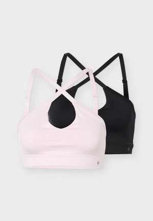 Femme en forme portant un soutien-gorge de sport rose, un short violet, des chaussettes blanches et des baskets, tenant une bouteille d'eau noire, portant des gants d'entraînement noirs.