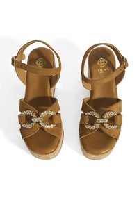 Beige Wildledersandalen mit Plateau und Korksohle, ausgestattet mit einer dekorativen, verzierten metallischen Schnalle. Verstellbarer Knöchelriemen inklusive.