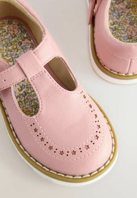 Rosa Leder Mary Jane Schuhe mit T-Riemen, durchbrochenen Sternmustern und floralem Innensohle. Weiße Sohle mit gelben Akzenten.