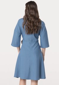 Robe bleue à manches trois-quarts, taille cintrée et jupe évasée. Tissu doux, minimalisme dans les détails et texture lisse.