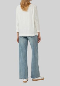 Witte lange mouwen top met een relaxte pasvorm en een ronde halslijn, gecombineerd met lichtblauwe wijde jeans en witte sneakers.