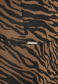 Materiał w brązowy i czarny wzór w paski przypominający tygrysa, z teksturowanym wykończeniem, posiadający mały metaliczny emblem marki.