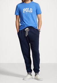 Blå bomulls t-shirt med "POLO RALPH LAUREN"-logotyp, kombinerad med mörkblå sweatpants och off-white sneakers med gråa accenter.