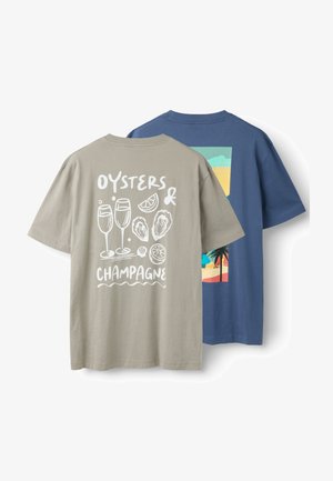 Dos camisetas de manga corta, una beige con ostras blancas, copas de champán, limón y el texto "Oysters & Champagne", y una azul con una escena de playa.