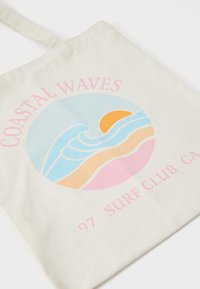Sac fourre-tout en toile de couleur naturelle présentant un graphique rond avec des vagues en bleu, rose et orange, ainsi que le texte "COASTAL WAVES 97 SURF CLUB CA".