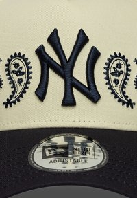 Șapcă de baseball ajustabilă, în crem și bleumarin, cu un logo brodat NY și modele paisley pe față, având o vizor neagră.