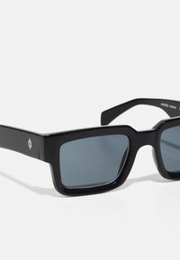 Black rectangular sunglasses with grey lenses. Made from smooth acetate, featuring a minimal logo on the temple. Angular frame design.