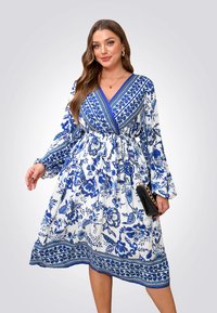 Blauwe en witte bloemenjurk met lange mouwen, V-hals en een cinched taille. Gedetailleerde patronen langs de zoom en een zwarte clutch tas.