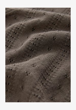 Tumma ruskea neulottu kangas, jossa on kuvioitu rakenne ja pieniä silmukkadetaljeja, jotka luovat hillityn ja hengittävän ilmeen.