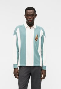 Πόλο πουκάμισο με μακρύ μανίκι, με κάθετες ρίγες σε τιρκουάζ και λευκό χρώμα, με γιακά και κεντημένο λογότυπο στο στήθος. Κατασκευασμένο από βαμβακερό υλικό, σε άνετη εφαρμογή.