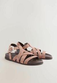 Sandali in suede rosa con fasce, suola nera piatta e chiusura a fibbia. Presentano più fasce incrociate e un design aperto sulla punta.
