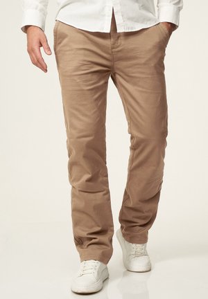 Beige Baumwollchinos mit geradem Bein, ausgestattet mit Seitentaschen und einer glatten Textur, kombiniert mit weißen Sneakers.