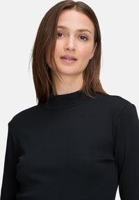 Schwarzes, geripptes Langarmoberteil mit hohem Kragen und figurbetonter Silhouette, das eine glatte Textur und minimale Nähte für ein elegantes Aussehen aufweist.
