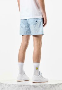Lysblå shorts lavet af let materiale, med to baglommer med sorte knapper, der er sat sammen med hvide sneakers og smiley sokker.