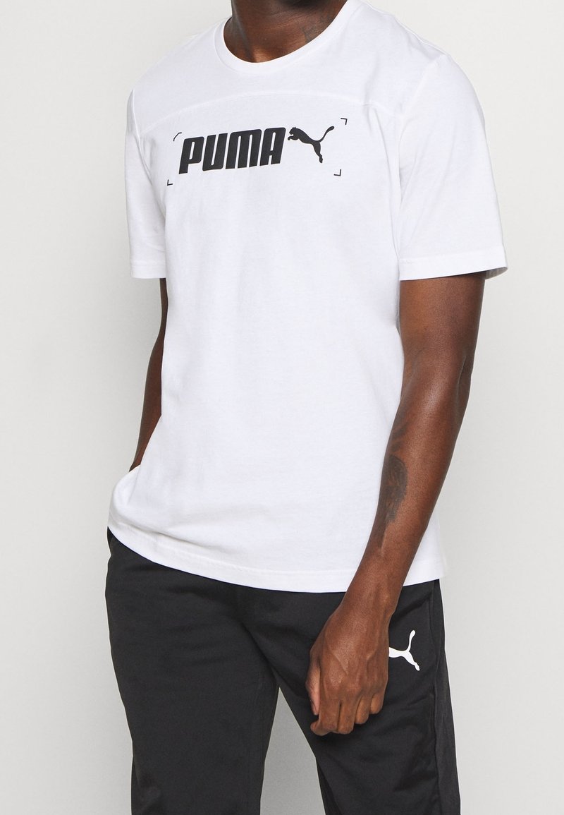 Camiseta blanca de manga corta con un audaz logo negro de "PUMA" en el pecho y un pequeño icono negro del gato Puma en la manga izquierda.
