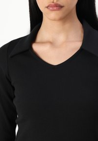 Μαύρη ριγέ μπλούζα με μακριά μανίκια, V-λαιμόκοψη και μυτερό γιακά, με ομαλή υφή και εφαρμοστή γραμμή.