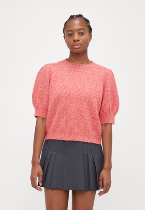 Kurze, croppende Strickjacke in einem lebhaften roten Knit mit strukturiertem Finish. Kombiniert mit einem plissierten, dunkelgrauen Rock.
