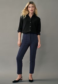 Cămașă neagră cu dungi albe, purtată cu pantaloni dark blue, ajustați. Ținuta este completată de pantofi slingback negri.