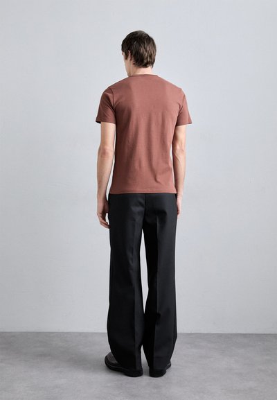 Camiseta marrón de manga corta combinada con pantalones anchos negros. El conjunto tiene un corte relajado y presenta líneas simples y limpias.