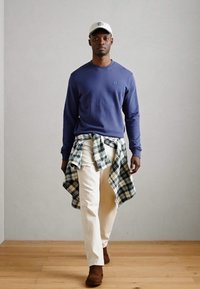 Modra srajca z dolgimi rokavi, smetana hlače, zelena in bela karirana srajca zavezana okoli pasu, rjavi čevlji in bela kapa.