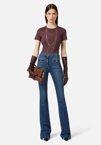 Top aderente marrone, jeans svasati blu a vita alta, guanti in pelle marroni, collana con catena dorata e pochette marrone con dettaglio a scatto.