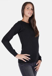Maglione lungo nero a maglia, con maniche lunghe, scollo rotondo, vestibilità slim e polsini a costine, abbinato a jeans scuri. Tessuto liscio, senza motivi.