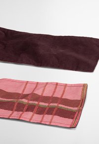 Dois pedaços de tecido: uma tira de corduroy bordô por cima e uma tira de xadrez rosa e castanho por baixo, apresentando texturas em nervuras e cores contrastantes.