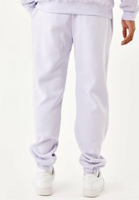 Lavendel sweatpants gemaakt van zacht materiaal, met ribbels aan de boorden en zijzakken, gecombineerd met witte sneakers.