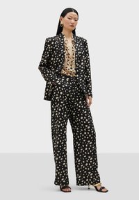 Sako s čiernymi a krémovými bodkami a široké nohavice, kombinované s krémovou blúzkou. Hladká látka a uvoľnený strih, s sandálmi na otvorenej špičke.