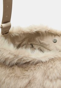 Faux fur -laukkua, jossa on vaaleanbeige ulkopinta ja pehmeä pinta. Laukussa on sileä sisävuori ja vetoketjullinen tasku. Säädettävä olkahihna kuuluu pakettiin.