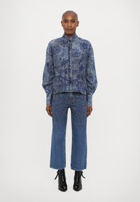 Denim shirt with a floral pattern, paired with high-waisted flared jeans featuring studded accents. Black ankle boots complete the look.