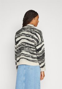 Gestrickter Pullover in Schwarz und Creme mit einem Zebrastreifenmuster. Verfügt über einen hohen Kragen und eine lockere Passform, gefertigt aus weichem, strukturiertem Material.