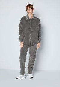 Grijze ribfluwelen shirt met knopen en bijpassende broek, beide met een ribbelstructuur. Sneakers maken de outfit af.